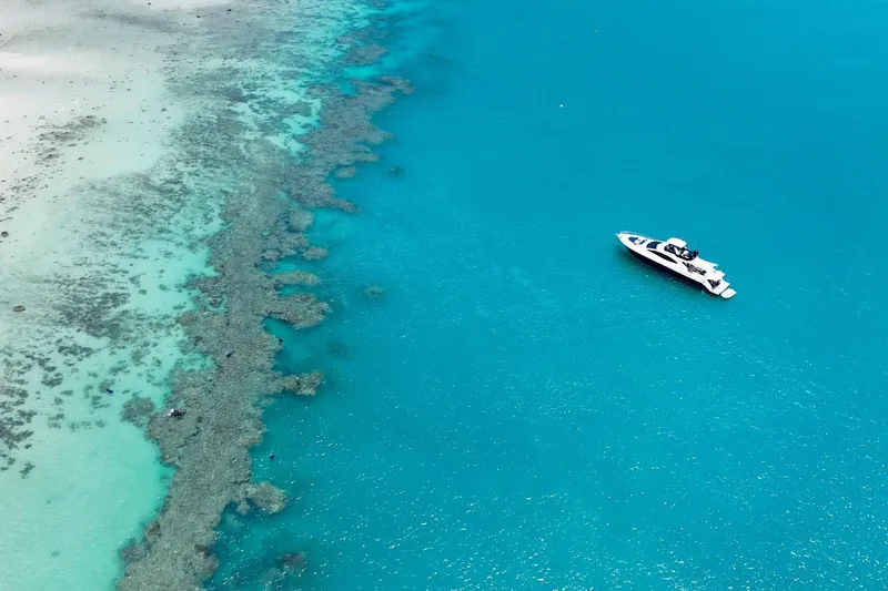 La Mar Yacht Photos Pics Aerial view of 2012 Lazzara LSX 78 yacht in turquoise ocean near coral reef.