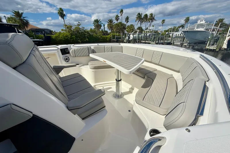  Yacht Photos Pics 2023 Pursuit S 358 Sport boat interior with luxurious seating and table, docked near palm trees.