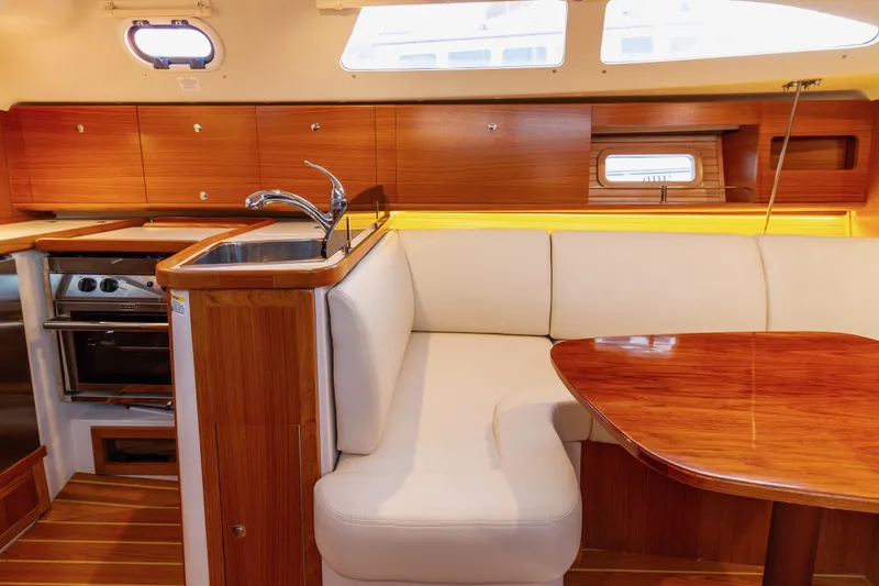 Nordlys Yacht Photos Pics 2018 Catalina 315 yacht interior with wooden cabinetry, white seating, and compact kitchen area.