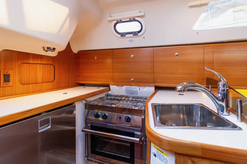 Nordlys Yacht Photos Pics 2018 Catalina 315 yacht kitchen with wood cabinets, stainless steel sink, and stove.