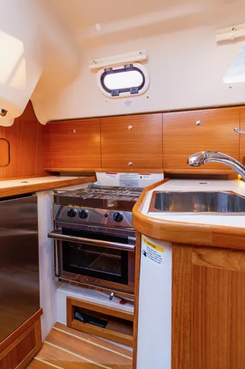 Nordlys Yacht Photos Pics 2018 Catalina 315 yacht kitchen with wood cabinetry, stainless steel stove, and sink.