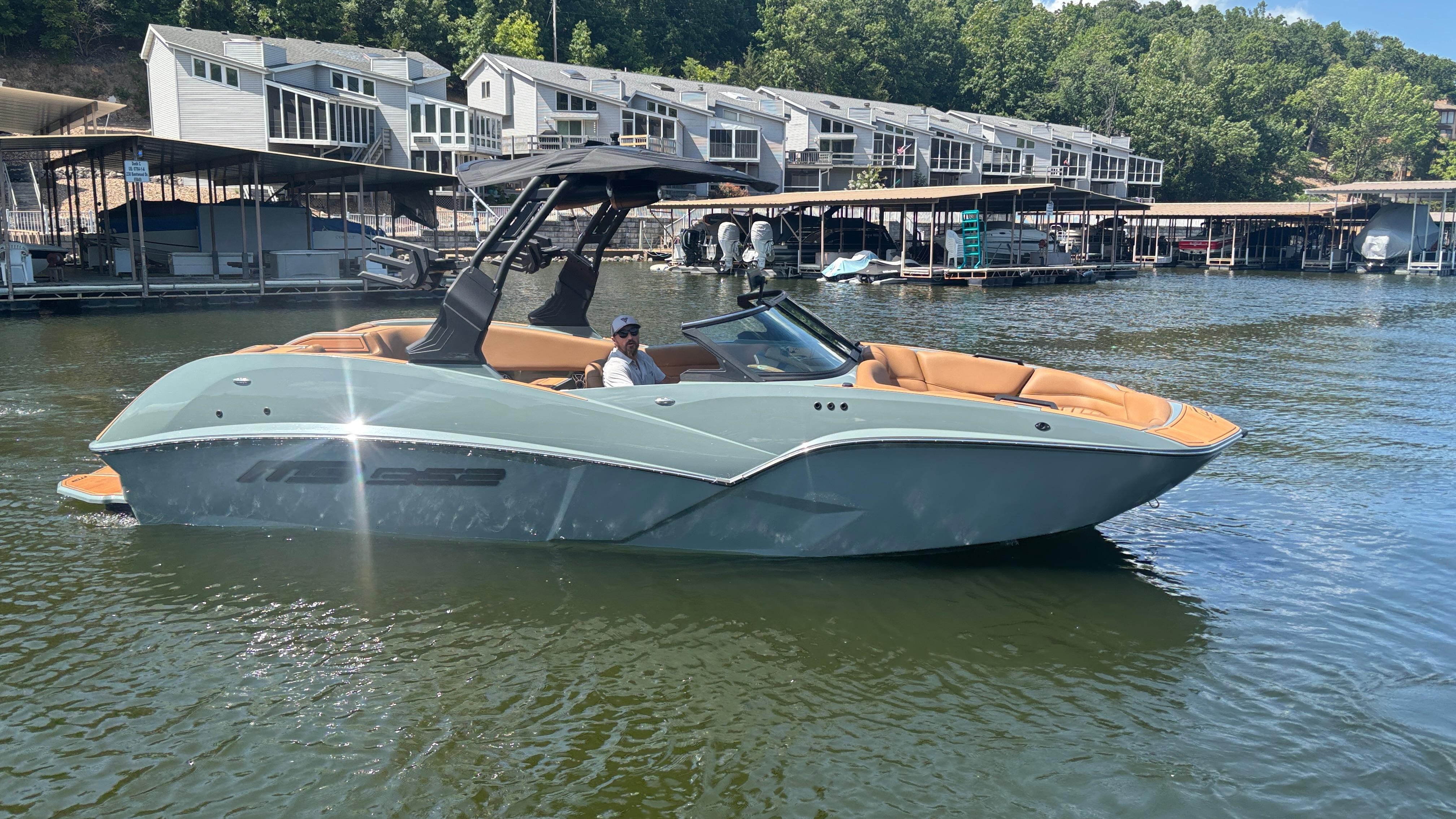 2025 MB B52 25 Alpha boat on a lake near modern waterfront homes.