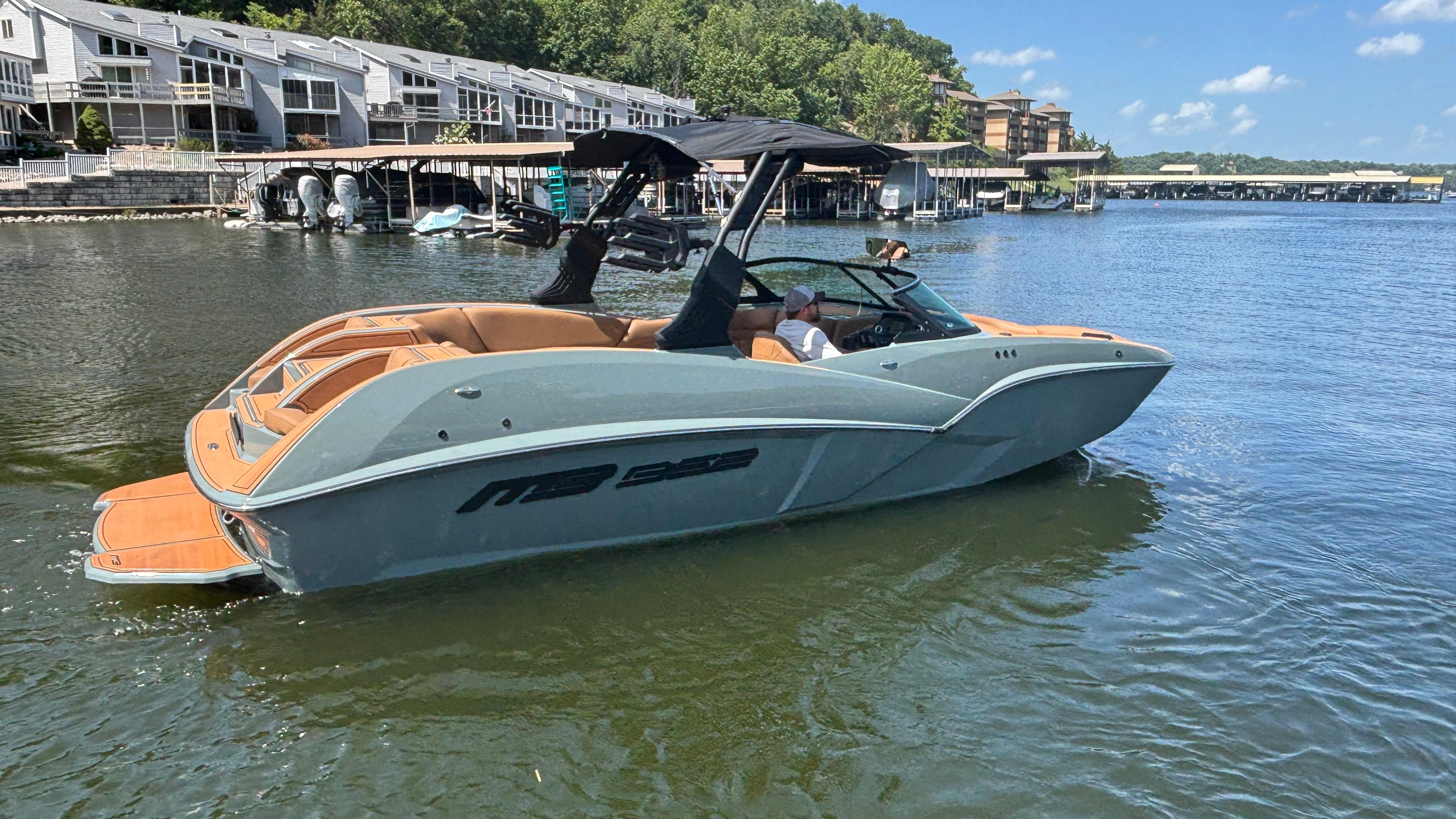 2025 MB B52 25 Alpha boat on a lake near waterfront homes.