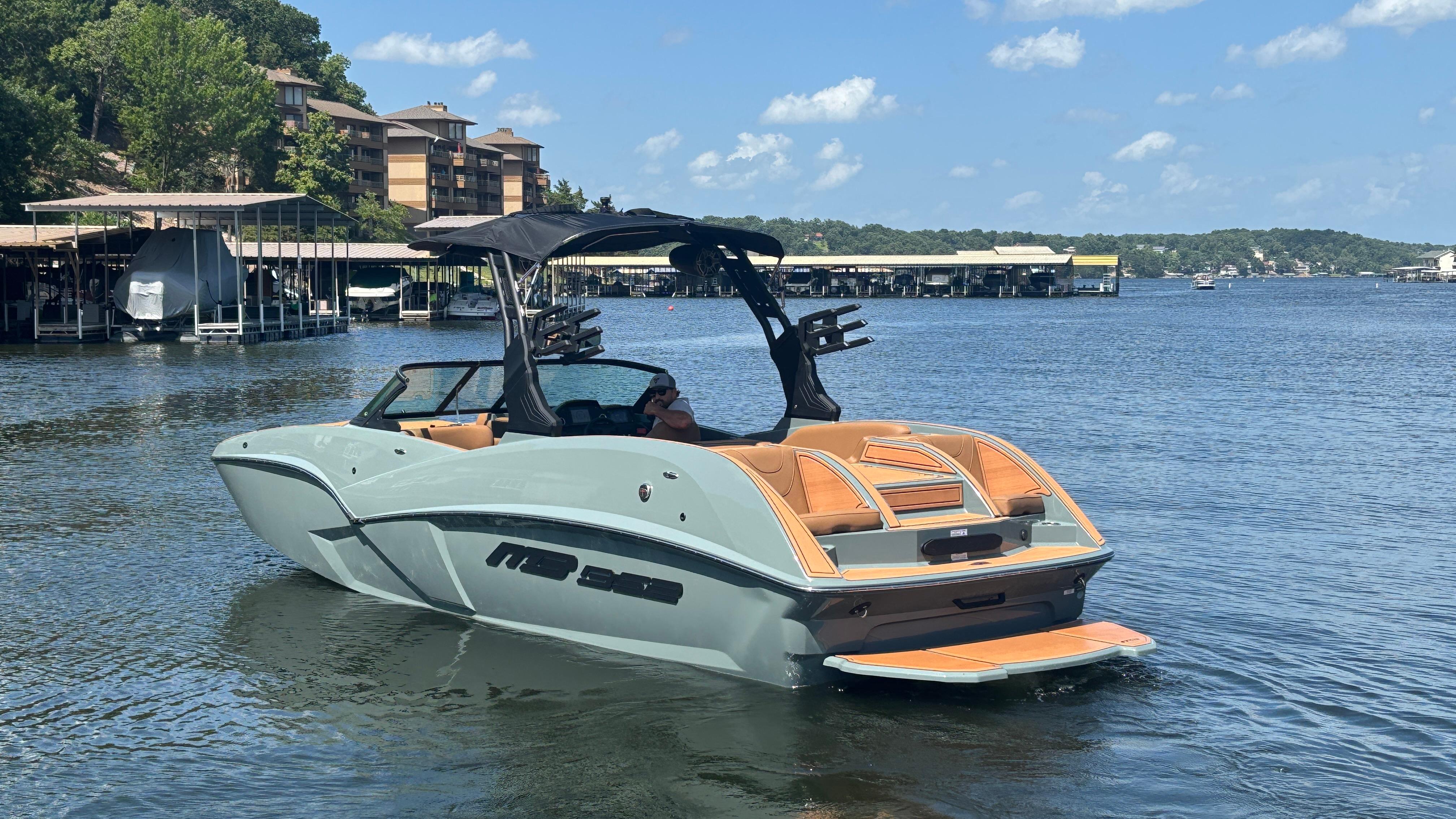 2025 MB B52 25 Alpha boat on a scenic lake with docks and buildings.