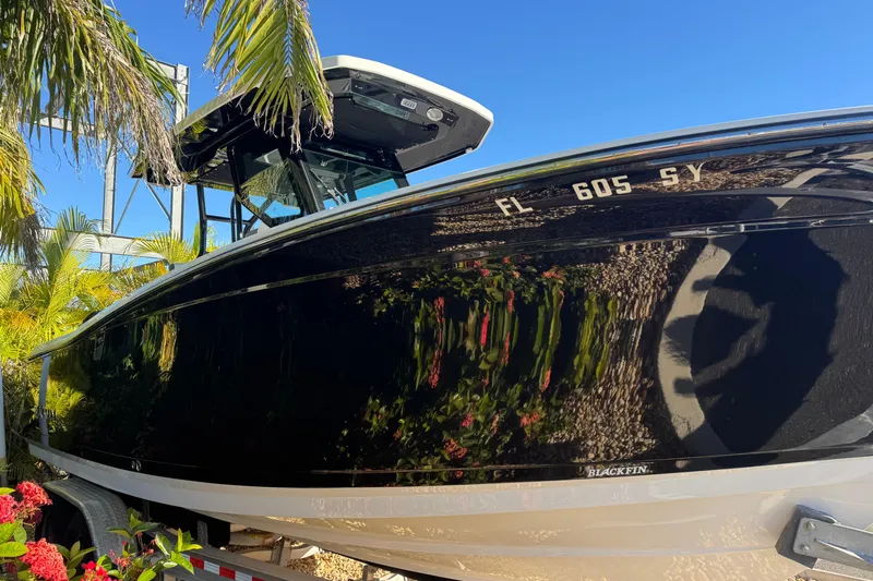  Yacht Photos Pics 2021 Blackfin 272 CC boat with sleek black hull, surrounded by tropical plants.