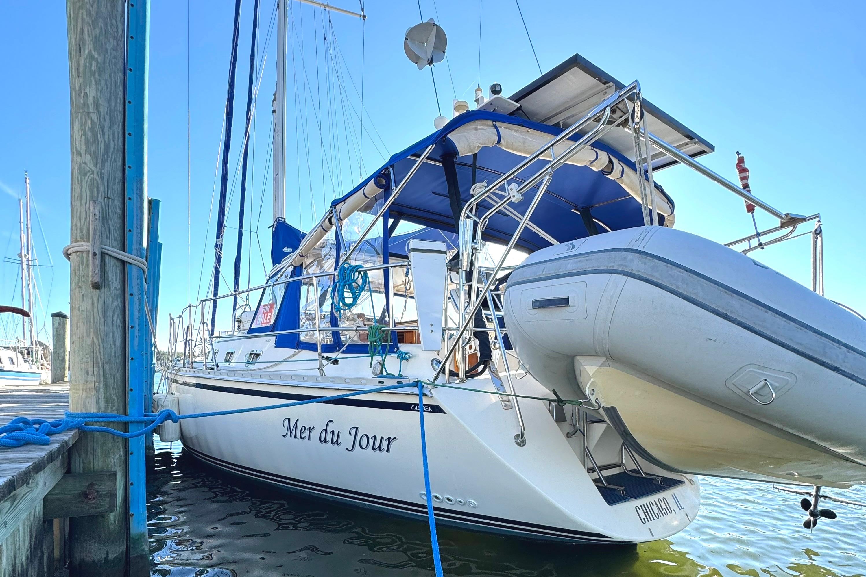 2005 Caliber 40 LRC SE sailboat docked with blue canopy and dinghy attached.