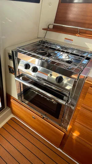  Yacht Photos Pics 2023 Ranger Tugs R-27 boat kitchen with stainless steel stove and oven, wooden cabinetry.