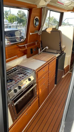 Yacht Photos Pics 2023 Ranger Tugs R-27 interior kitchen with wood cabinetry and modern appliances.