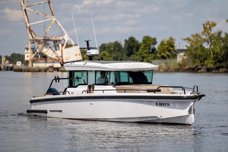 Yacht Photos Pics 2024 Axopar 37 XC boat cruising on a calm river with industrial backdrop.