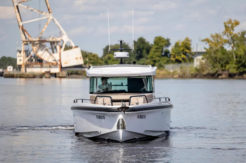  Yacht Photos Pics 2024 Axopar 37 XC boat cruising on a calm river near a rusty bridge.
