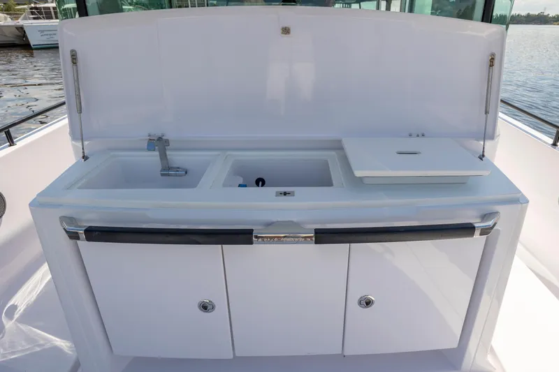  Yacht Photos Pics 2024 Axopar 37 XC boat kitchenette with sink and storage, docked by the water.