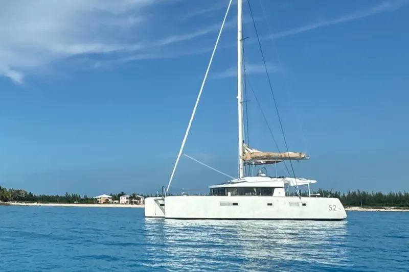 Nauti Adventure Yacht Photos Pics 2015 Lagoon 52 F catamaran sailing on clear blue waters near a sandy shoreline.