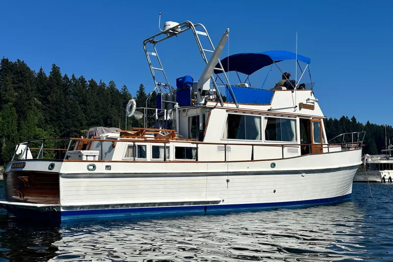  Yacht Photos Pics 1981 Grand Banks Classic Tri-cabin yacht on calm water, with blue canopy and wooded shoreline.