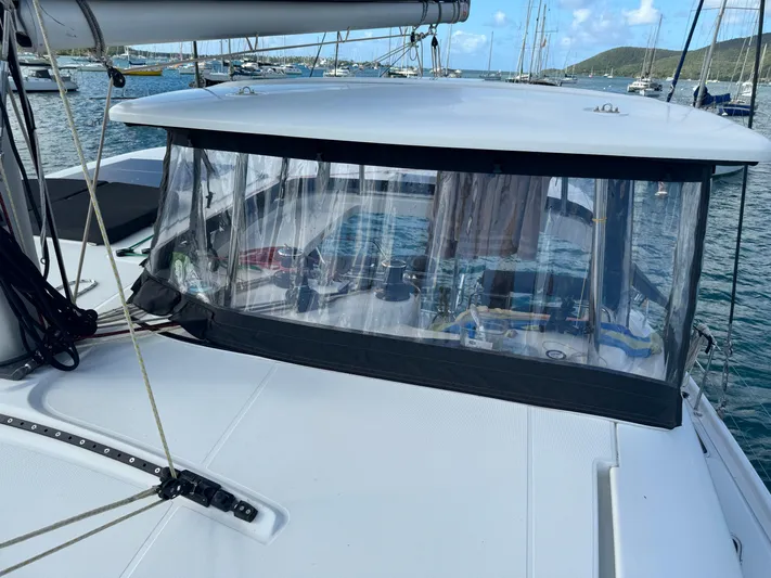 Solace Yacht Photos Pics 2020 Lagoon 42 catamaran with clear cockpit enclosure, docked in a scenic marina.