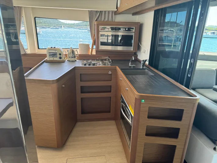 Solace Yacht Photos Pics Modern kitchen interior on a 2020 Lagoon 42 catamaran, featuring wood cabinetry and ocean view.