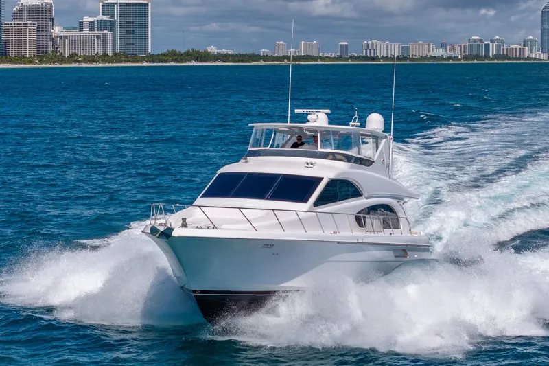 Starka Yacht Photos Pics 2009 Hatteras 64 Motor Yacht cruising on blue ocean near city skyline.