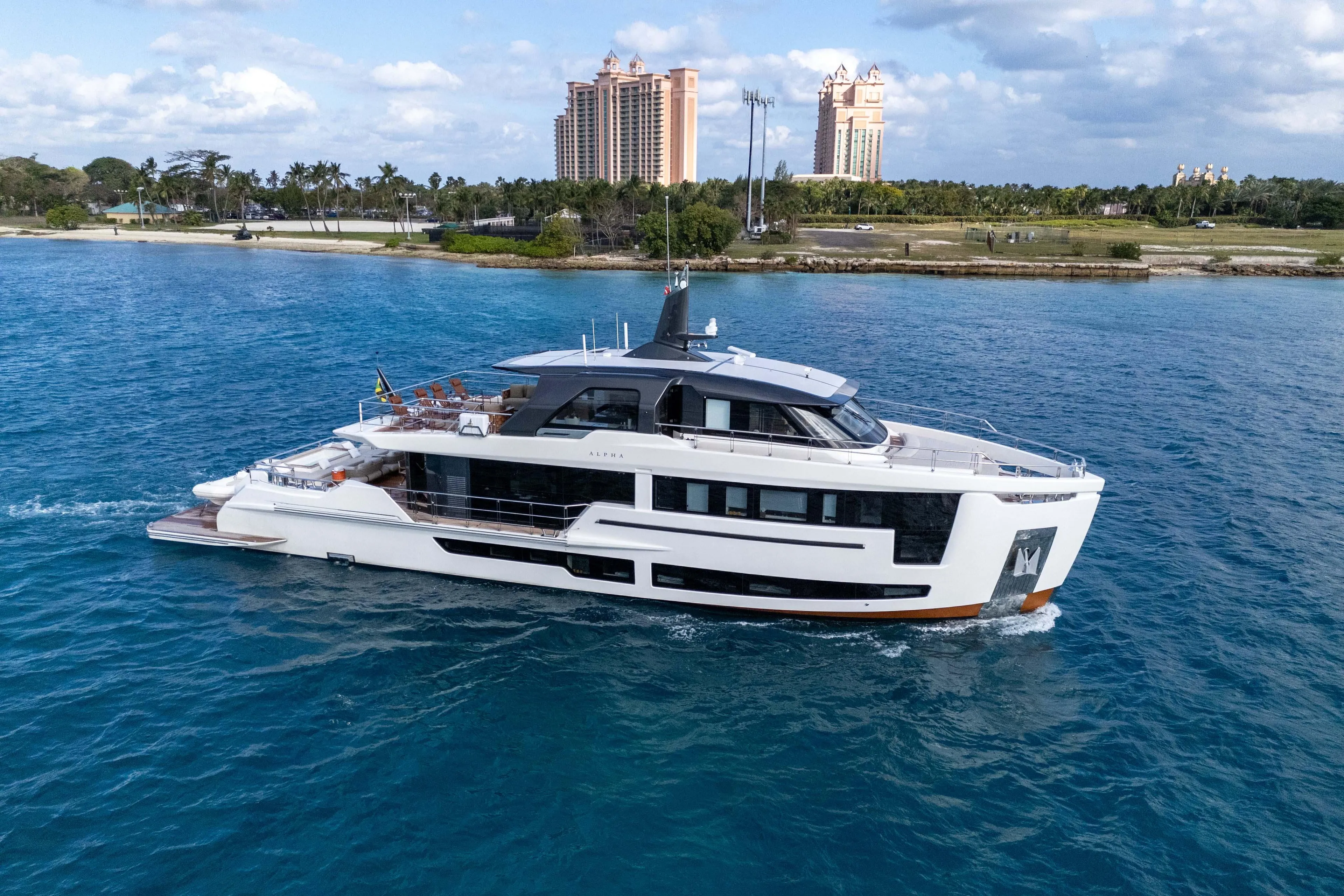 Luxurious 2025 Alpha Squalo Co Ownership yacht cruising in clear blue waters near a coastal cityscape.