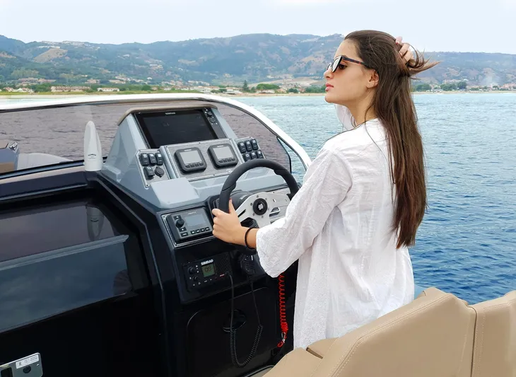  Yacht Photos Pics Woman steering 2025 Ranieri CAYMAN 28 EXECUTIVE boat on open water.