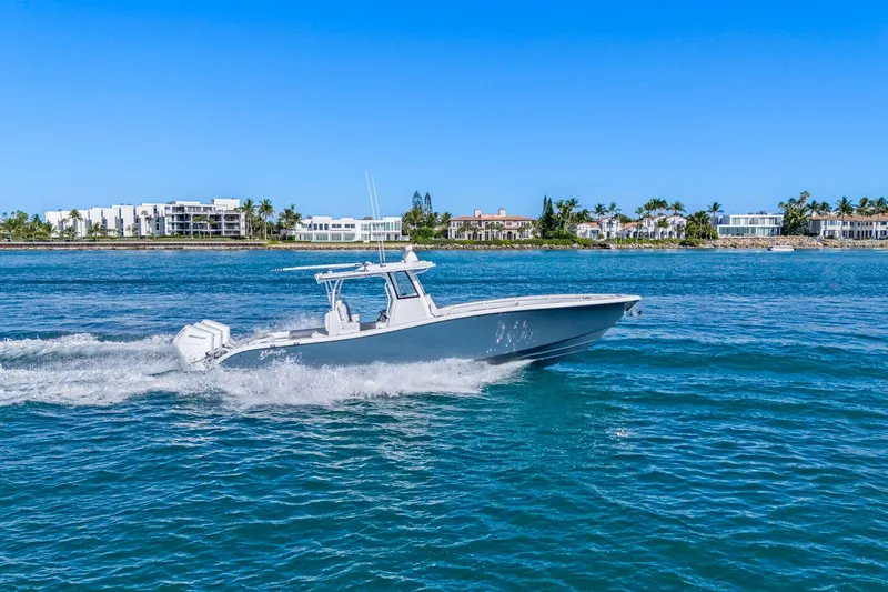 New Stock Yacht Photos Pics 2026 Yellowfin 36 Offshore boat cruising on clear blue water near a coastal cityscape.