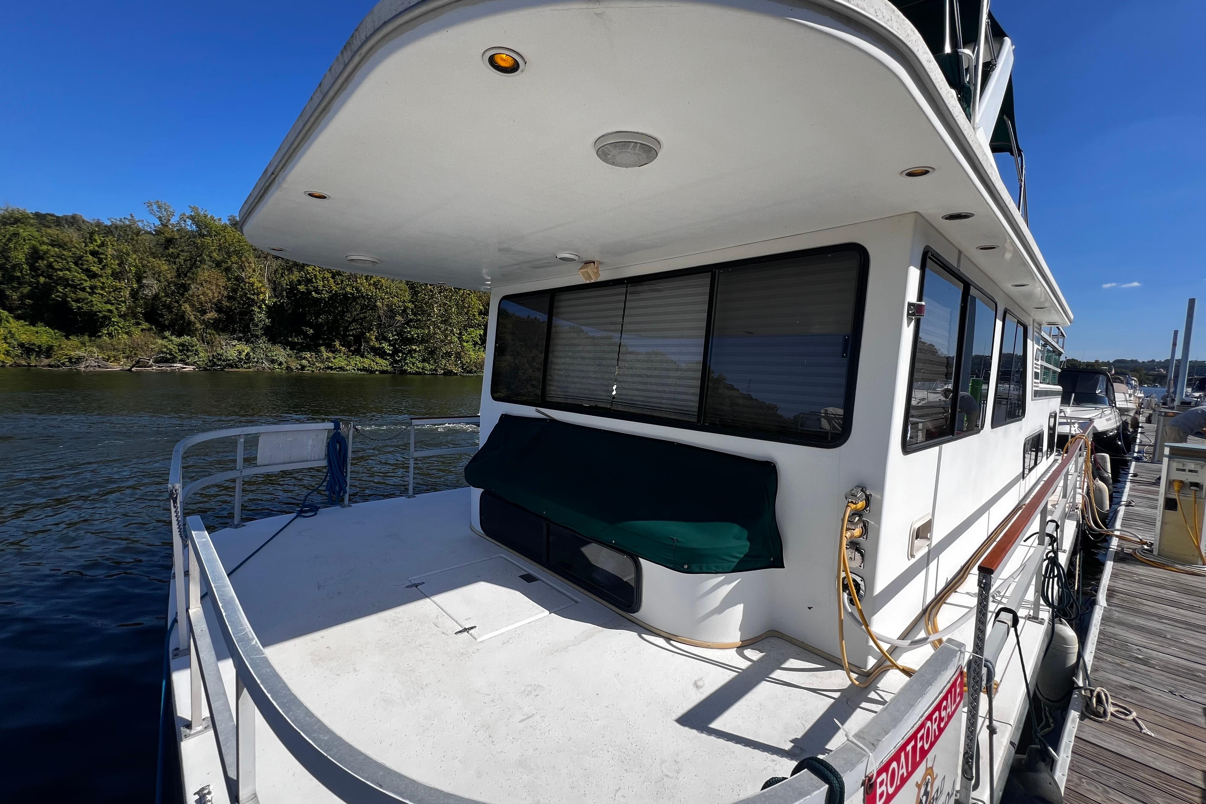 1994 Gibson 44 Classic houseboat docked by a scenic river under a clear blue sky.