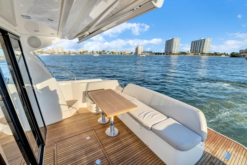 E Komo Mai Yacht Photos Pics Luxurious 2022 Prestige 420S yacht deck with seating, overlooking a scenic waterfront cityscape.