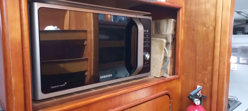 Zarafet Yacht Photos Pics Microwave in a 1995 Prout 45 yacht kitchen, with wooden cabinetry and a fire extinguisher nearby.