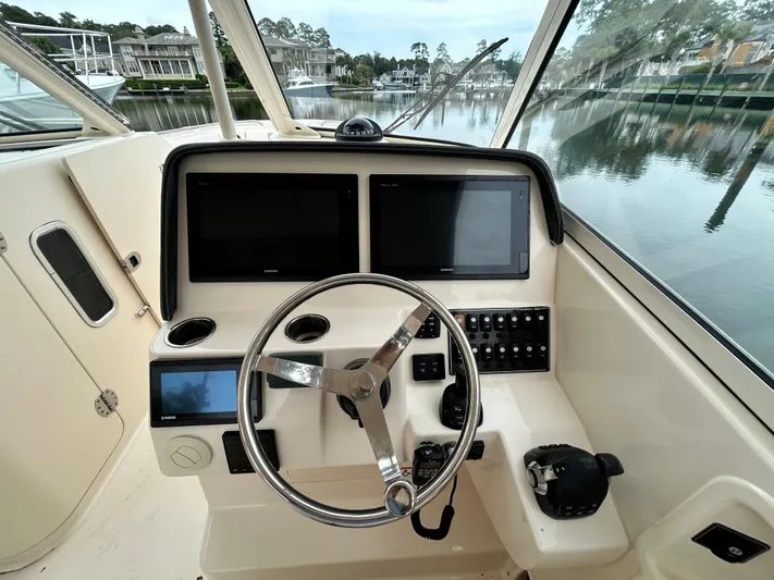  Yacht Photos Pics 2018 Grady-White Freedom 325 boat helm with dual screens and steering wheel, docked by calm waters.