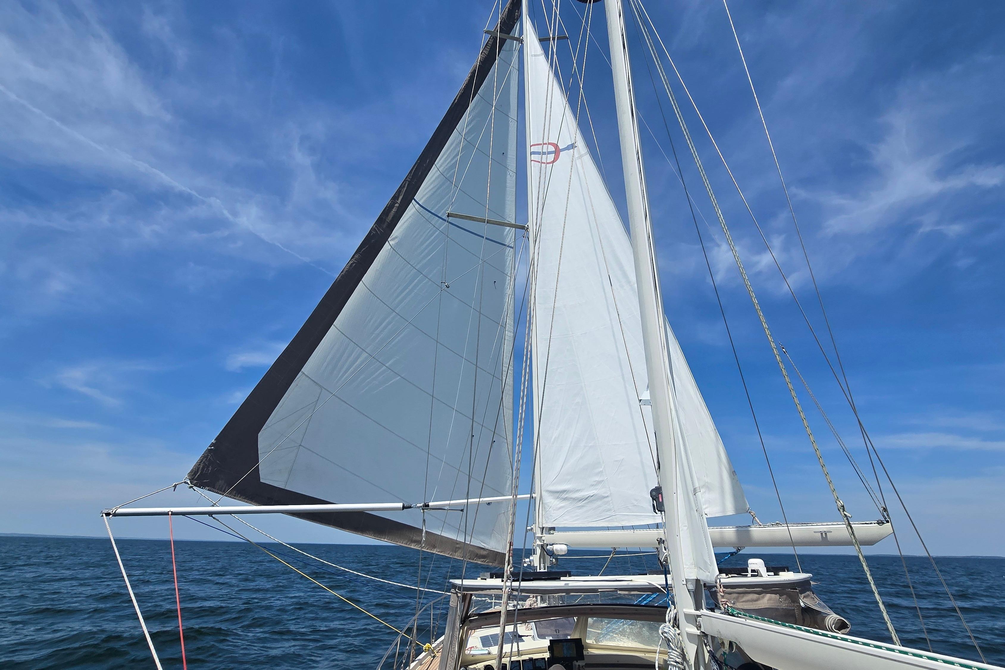 Sailing yacht Amel Santorin 1993 with sails unfurled on open sea under blue sky.