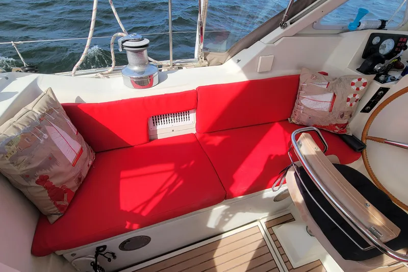 Omorfi Thea Yacht Photos Pics Cozy cockpit of 1993 Amel Santorin sailboat with red cushions and nautical-themed pillows.