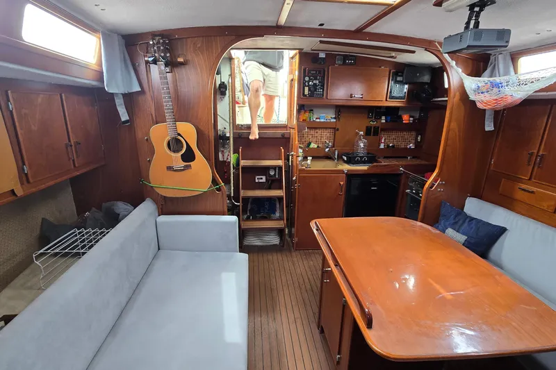 Omorfi Thea Yacht Photos Pics Interior of 1993 Amel Santorin sailboat with wooden furnishings and guitar on wall.
