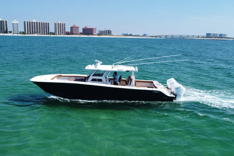  Yacht Photos Pics 2024 Invincible 46 Catamaran cruising on clear blue ocean near coastal city skyline.