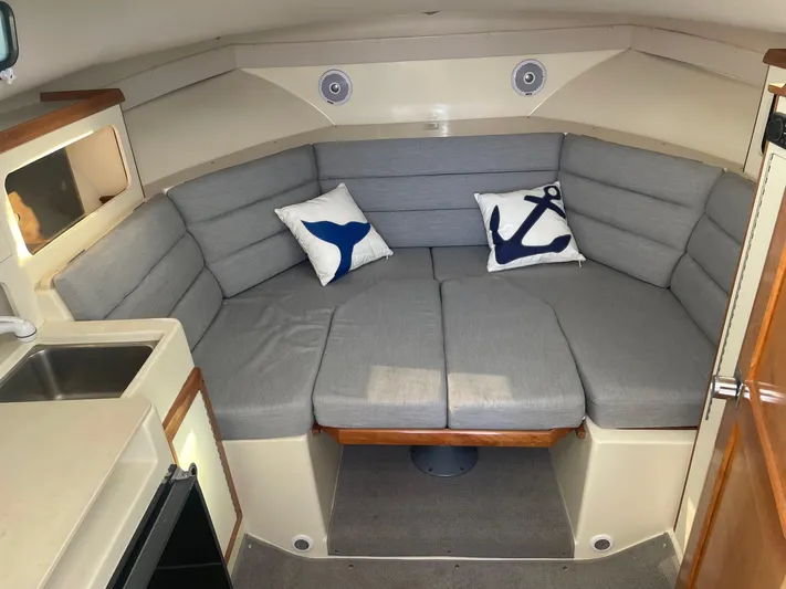 Five Belles Yacht Photos Pics 2001 Albin 28TE boat interior with gray seating, nautical pillows, and compact kitchenette.