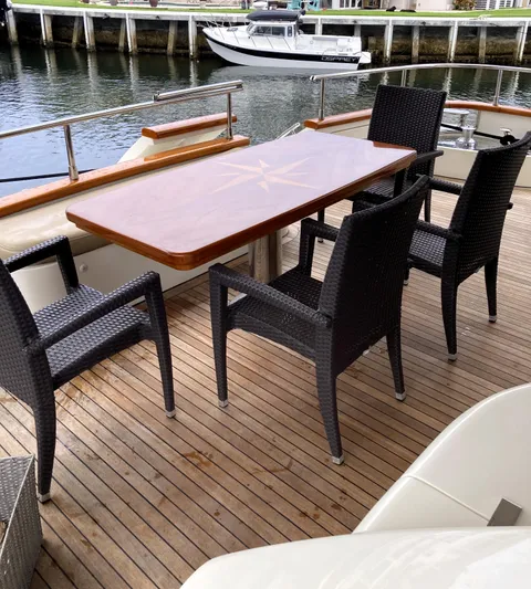 Dreamer Yacht Photos Pics Outdoor dining area on 2005 Azimut 80 Carat yacht with wooden table and wicker chairs.