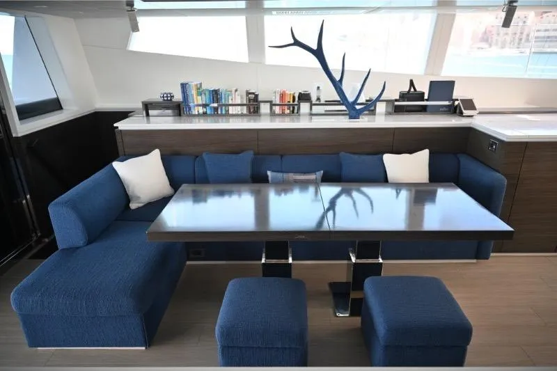  Yacht Photos Pics Luxurious Sunreef 74 yacht interior with blue seating, modern table, and decorative bookshelf.