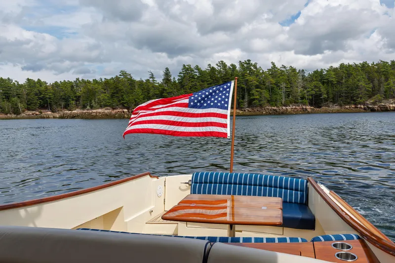The Do-over Yacht Photos Pics 2024 Hinckley Picnic Boat 40 with American flag on calm waters, forested shoreline.