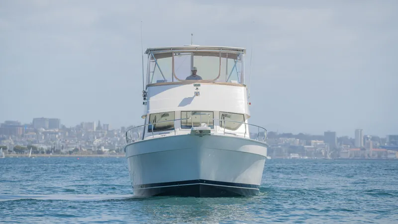 Temptation Yacht Photos Pics 2005 Mainship 43 Trawler Aft Cabin cruising on open water with city skyline backdrop.