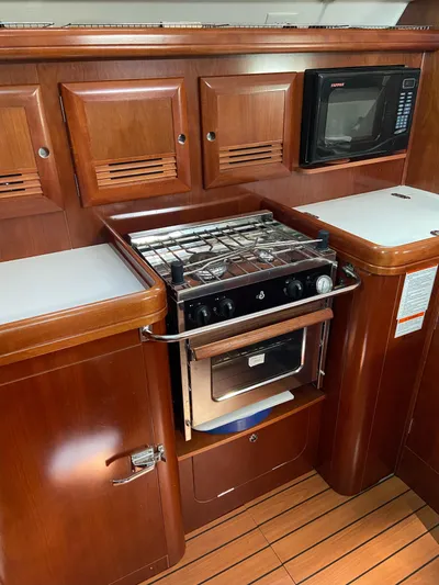 Windsome Yacht Photos Pics Galley kitchen in 2006 Beneteau Oceanis 373 sailboat with stove, microwave, and wooden cabinetry.