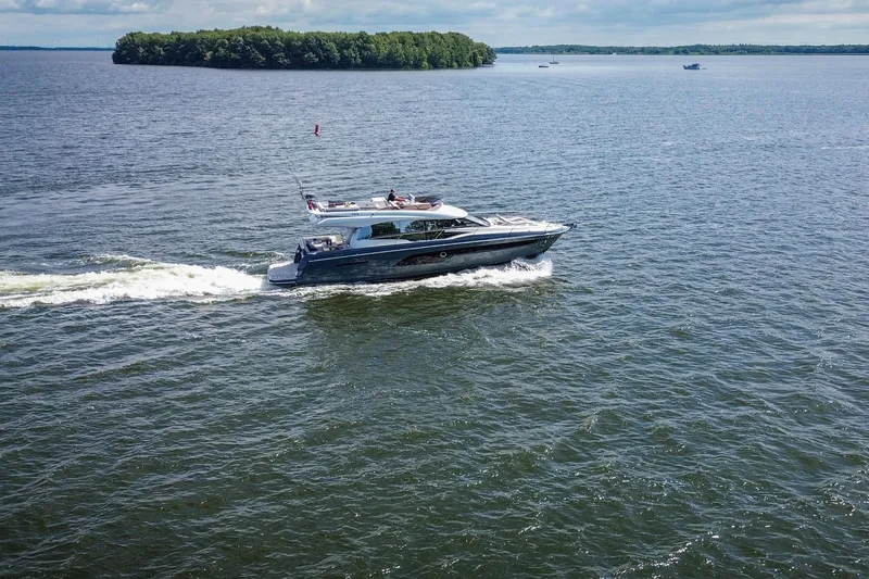  Yacht Photos Pics Luxury 2021 Prestige 520 yacht cruising on a serene lake with lush island backdrop.