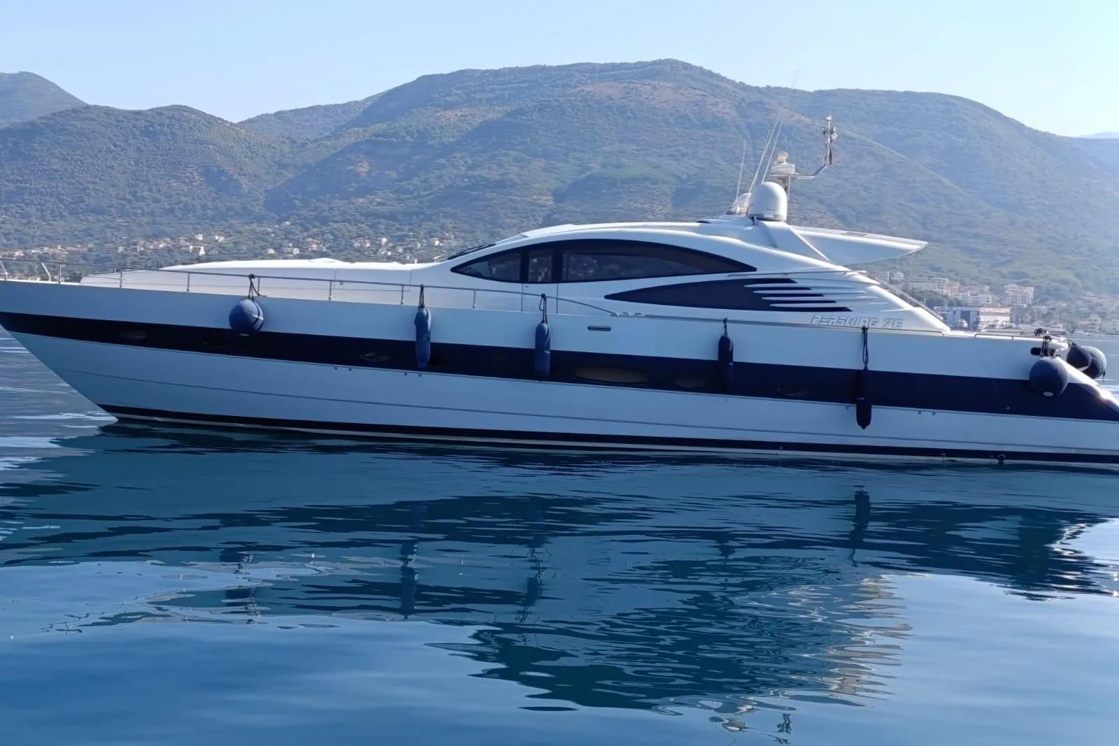 Luxury 2005 Pershing 76 yacht cruising on calm waters with scenic mountain backdrop.