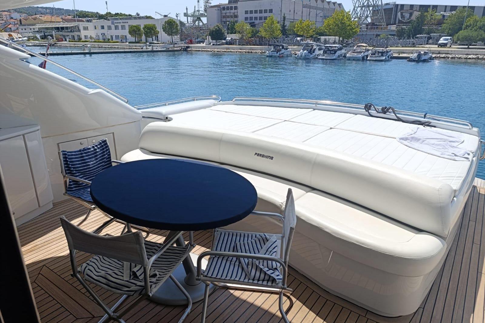 Luxury deck of 2005 Pershing 76 yacht with seating and table, docked by the water.