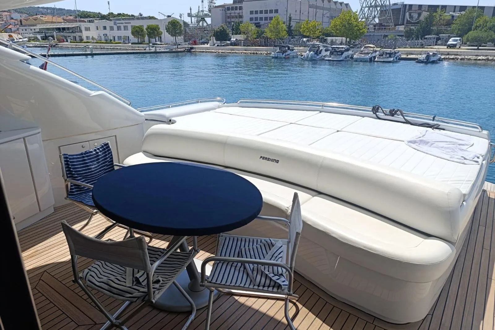 Luxury deck of 2005 Pershing 76 yacht with seating and table, docked by the water.