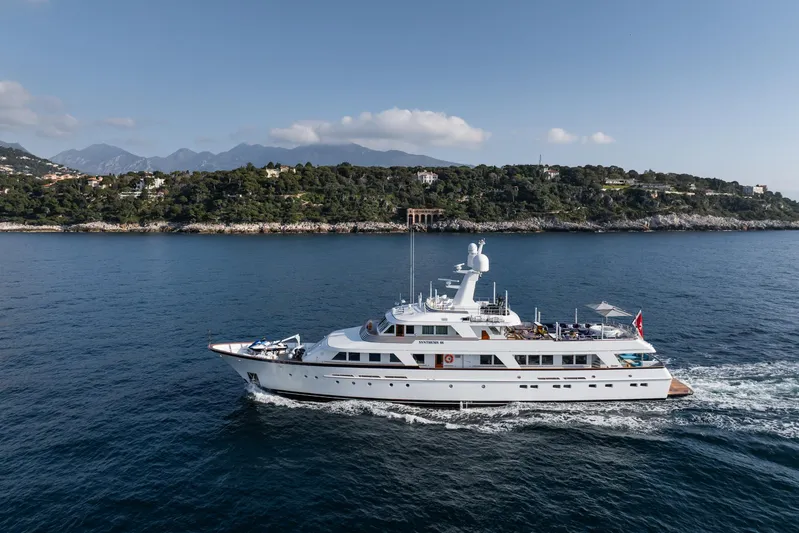 Synthesis 66 Yacht Photos Pics Luxurious 1982 Feadship yacht cruising near a scenic coastline under a clear blue sky.