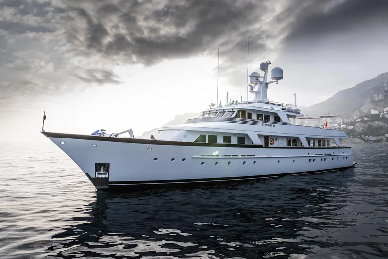 Synthesis 66 Yacht Photos Pics Luxurious 1982 Feadship yacht cruising under dramatic skies near a coastal landscape.
