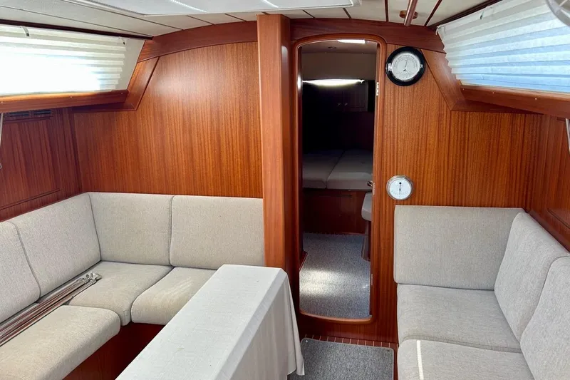 Magic I Yacht Photos Pics Interior of 2021 Hallberg-Rassy 44 yacht with wood paneling and beige seating.