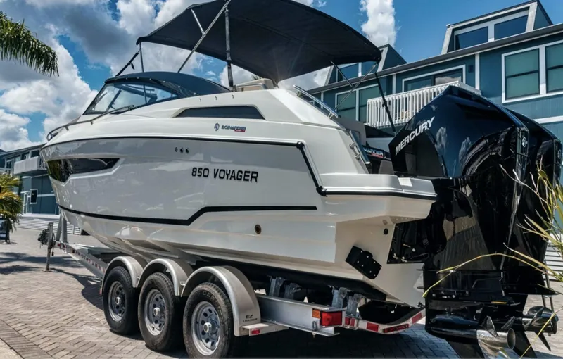  Yacht Photos Pics 2024 Skamander 850 Voyager boat on trailer, parked near modern buildings.