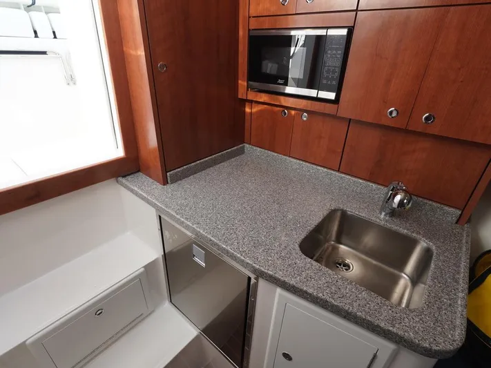  Yacht Photos Pics 2024 Albemarle 30 Express boat kitchen with sink, microwave, and wooden cabinetry.