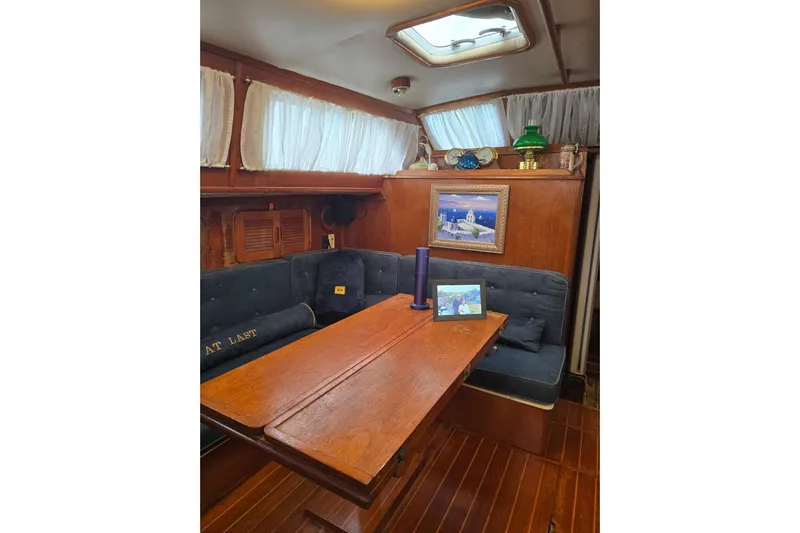At Last Yacht Photos Pics Cozy interior of 1982 Irwin 52 sailboat with wooden table and cushioned seating.