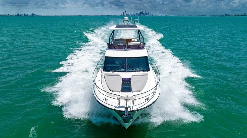 Grace Yacht Photos Pics 2022 Beneteau Monte Carlo 52 yacht cruising on turquoise water with city skyline in background.