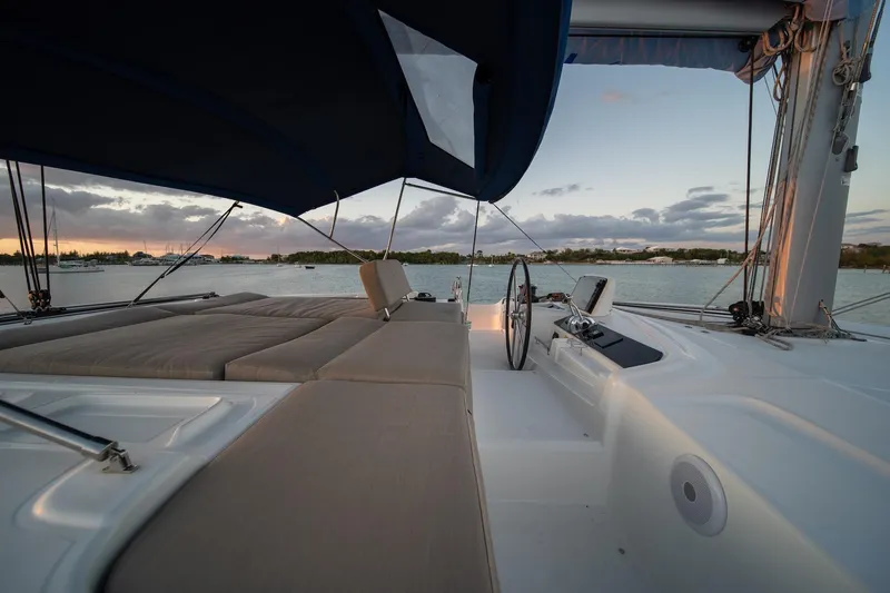 Watercolor Yacht Photos Pics 2023 Lagoon 46 catamaran deck with seating, steering wheel, and canopy at sunset.