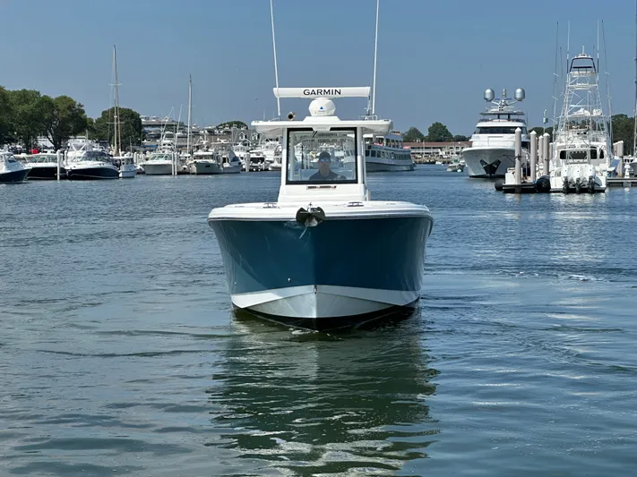  Yacht Photos Pics 2023 Edgewater 285CC boat navigating a marina, surrounded by yachts and calm water.